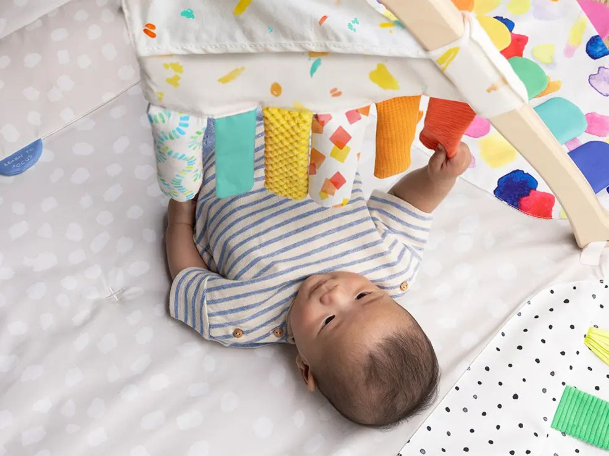 Un bebé tratando de alcanzar las tiras con colores. Esta es una de las mejores ideas para hacer juguetes de estimulación temprana