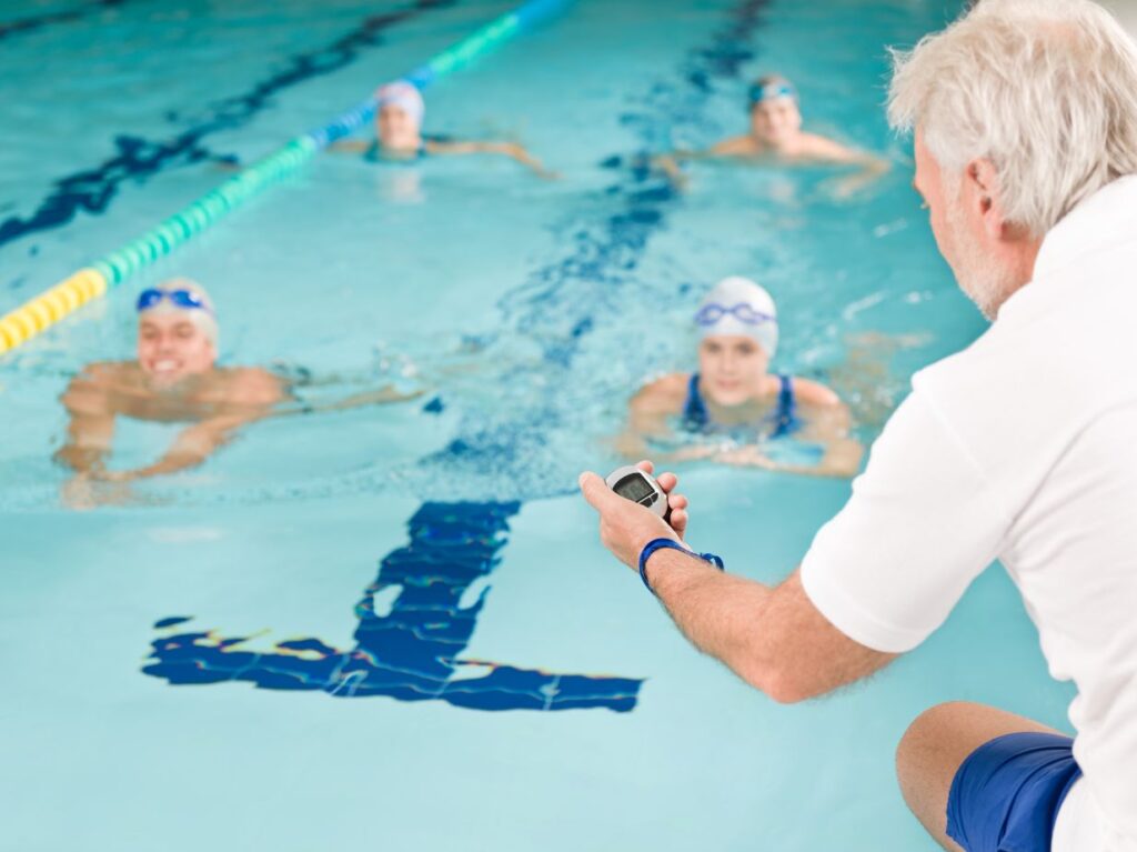 Personas en una competencia de natación, con un entrenador sacando tiempos