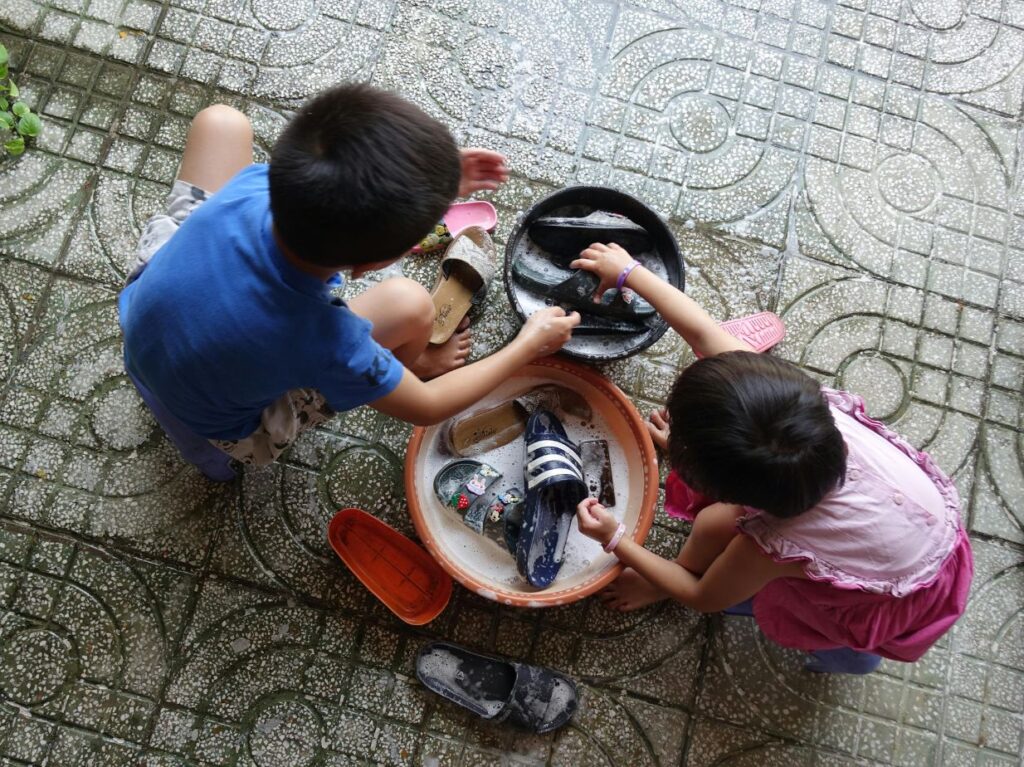 Niños lavando sus chanclas de manera lúdica, como si fuera adultos
