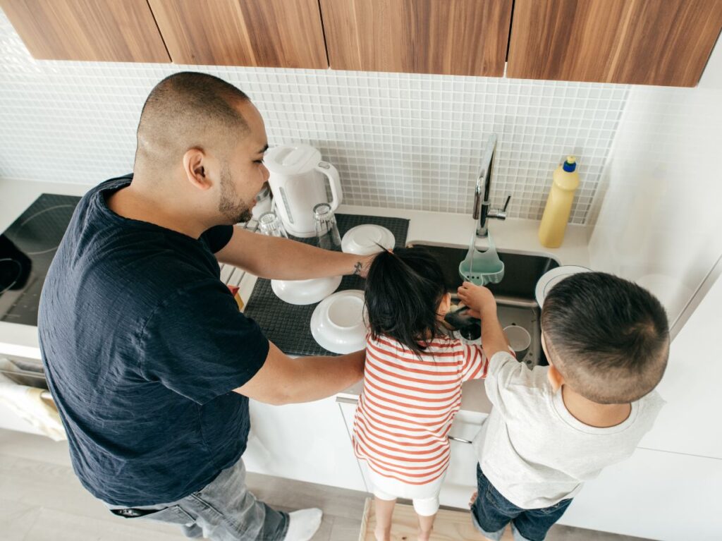 Un padre y sus dos hijos lavando trastes, porque los enseñó a desarrollar responsabilidad desde pequeños
